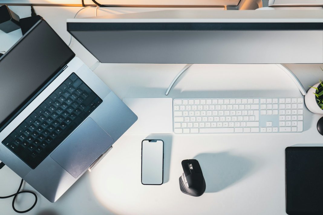 a desk with a laptop, keyboard, mouse and a cell phone